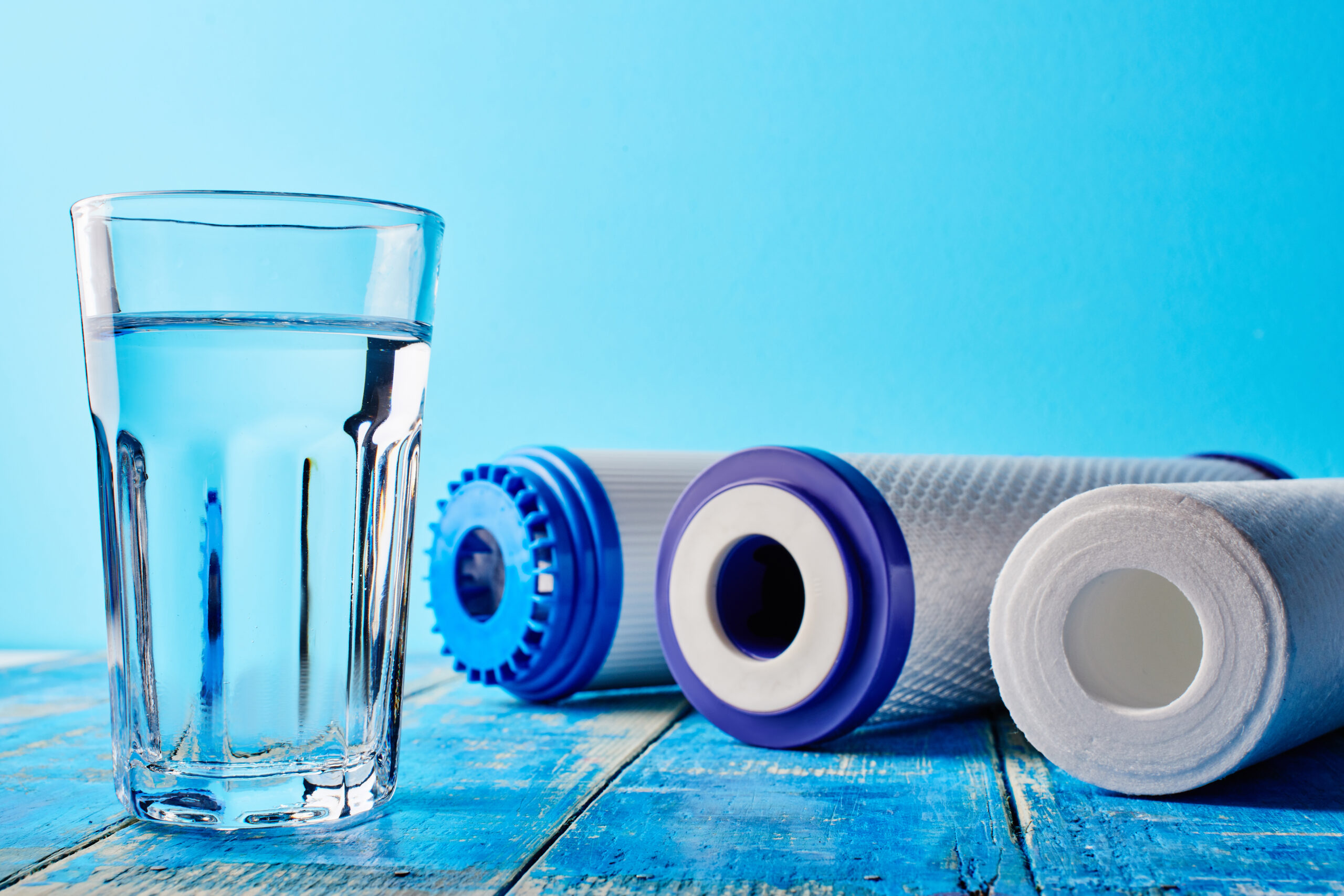 Water filters. Carbon cartridges and a glass on a blue background. Household filtration system.